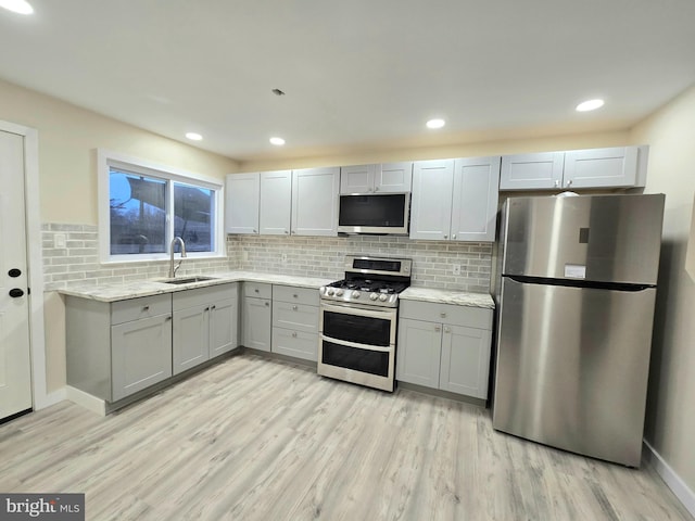 kitchen featuring sink, stainless steel appliances, light stone counters, light hardwood / wood-style flooring, and decorative backsplash