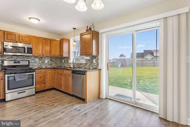 kitchen featuring pendant lighting, sink, light hardwood / wood-style flooring, appliances with stainless steel finishes, and tasteful backsplash