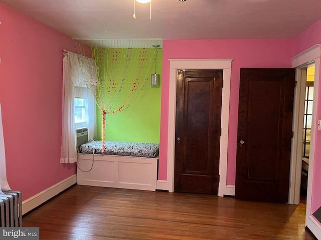 unfurnished bedroom featuring hardwood / wood-style floors, radiator, and cooling unit