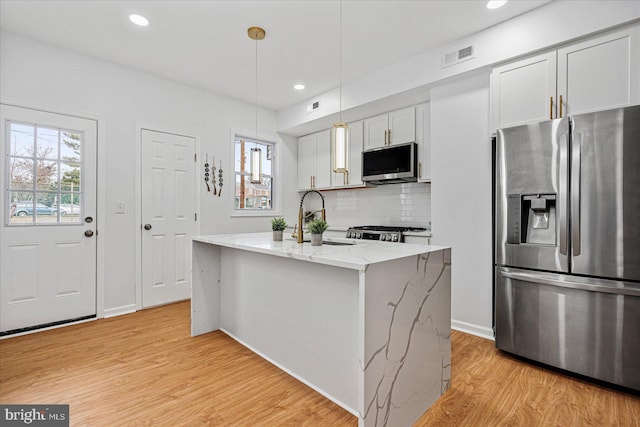 kitchen with white cabinetry, stainless steel appliances, light stone counters, light hardwood / wood-style floors, and decorative light fixtures