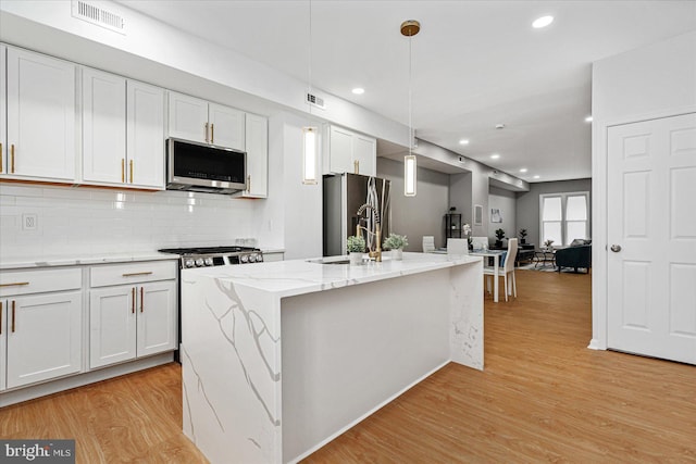 kitchen with white cabinets, light wood-type flooring, a kitchen island with sink, and appliances with stainless steel finishes