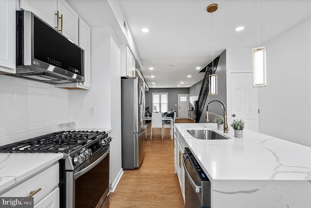 kitchen featuring white cabinets, sink, light wood-type flooring, appliances with stainless steel finishes, and decorative light fixtures