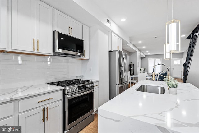 kitchen featuring white cabinets, sink, stainless steel appliances, and hanging light fixtures