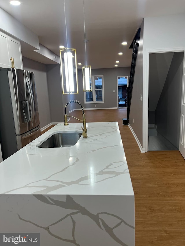 kitchen featuring light stone countertops, stainless steel refrigerator with ice dispenser, pendant lighting, and sink