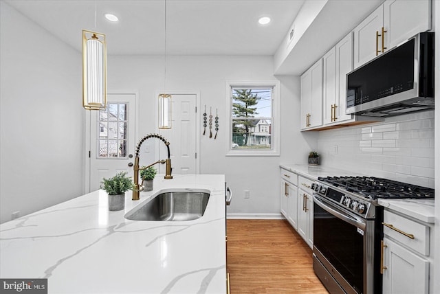 kitchen with light stone countertops, appliances with stainless steel finishes, pendant lighting, and sink