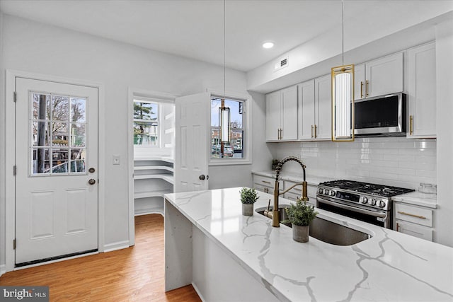 kitchen featuring light stone countertops, stainless steel appliances, white cabinets, and hanging light fixtures