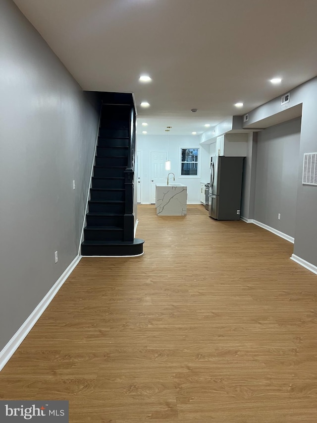 basement featuring light hardwood / wood-style floors, sink, and stainless steel refrigerator