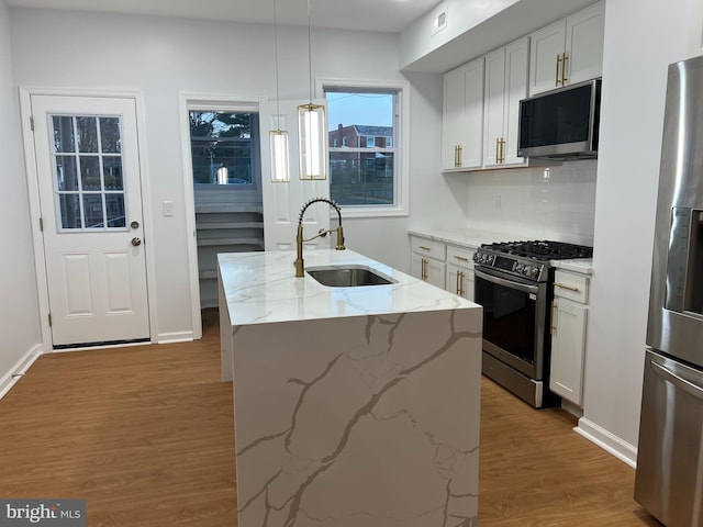 kitchen with a center island with sink, white cabinets, sink, appliances with stainless steel finishes, and light stone counters