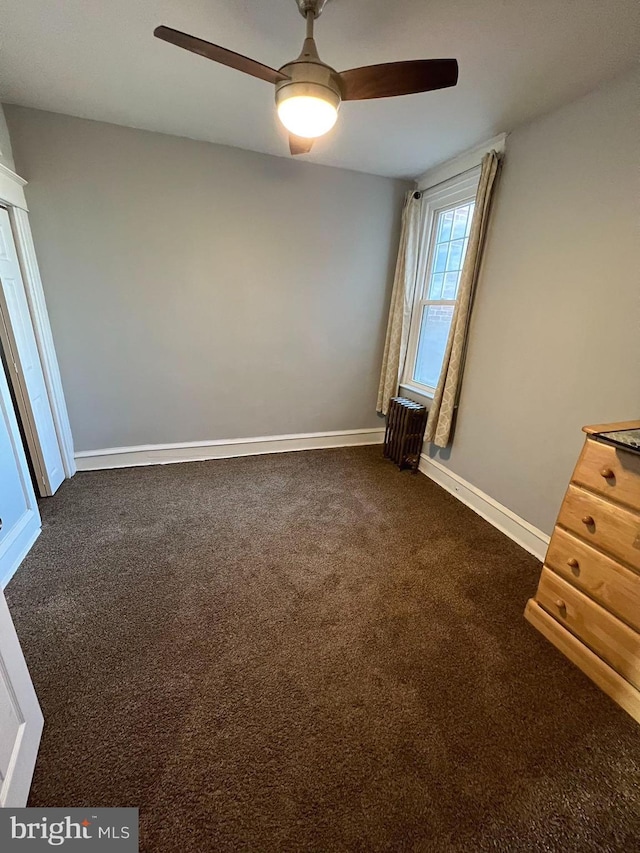 unfurnished bedroom with dark colored carpet, ceiling fan, and radiator heating unit