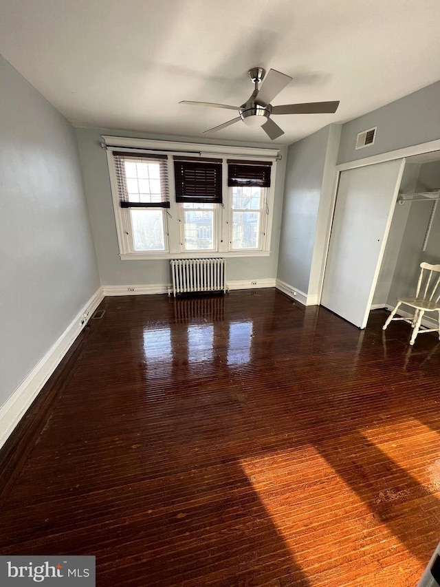 unfurnished living room with dark hardwood / wood-style floors, ceiling fan, and radiator heating unit