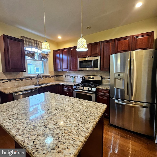 kitchen with decorative light fixtures, light stone countertops, sink, and appliances with stainless steel finishes