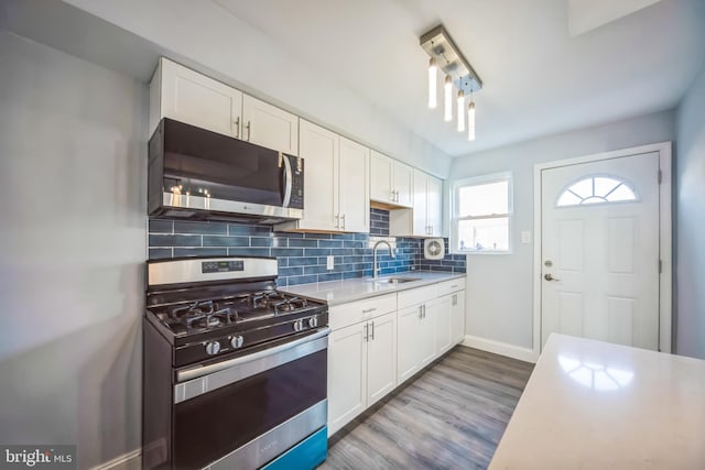 kitchen with backsplash, white cabinets, sink, hardwood / wood-style flooring, and stainless steel appliances