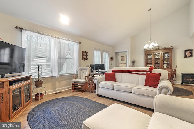 living room featuring a wealth of natural light, high vaulted ceiling, a chandelier, and light wood-type flooring