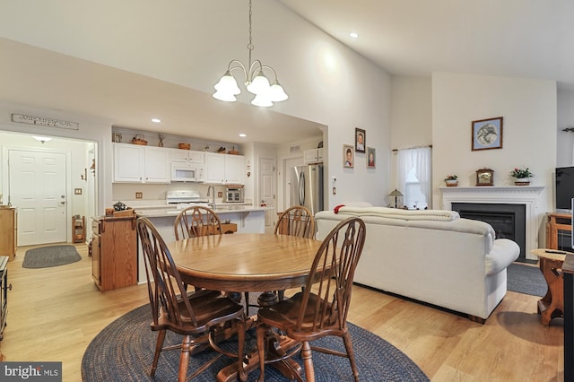 dining area with light hardwood / wood-style flooring, high vaulted ceiling, and a chandelier