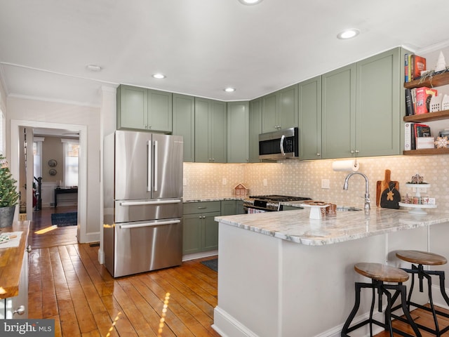 kitchen featuring light hardwood / wood-style floors, green cabinets, kitchen peninsula, and stainless steel appliances