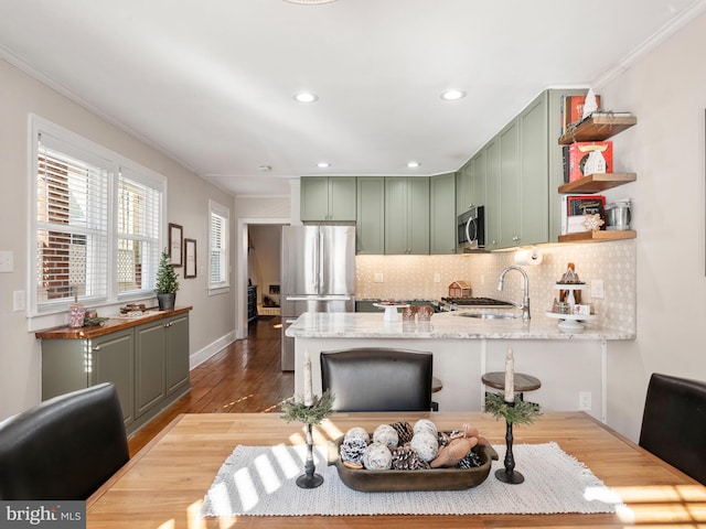 kitchen with kitchen peninsula, appliances with stainless steel finishes, sink, hardwood / wood-style flooring, and green cabinets