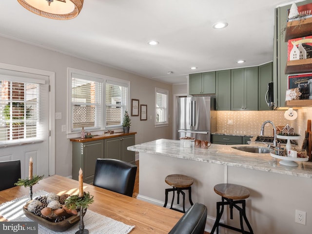 kitchen featuring a kitchen bar, light wood-type flooring, light stone counters, stainless steel appliances, and sink