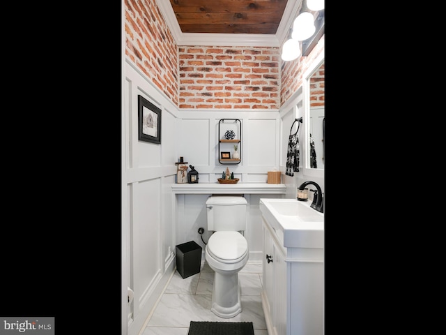 bathroom featuring vanity, toilet, crown molding, and brick wall