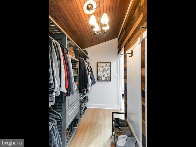 walk in closet featuring light hardwood / wood-style flooring, lofted ceiling, and an inviting chandelier