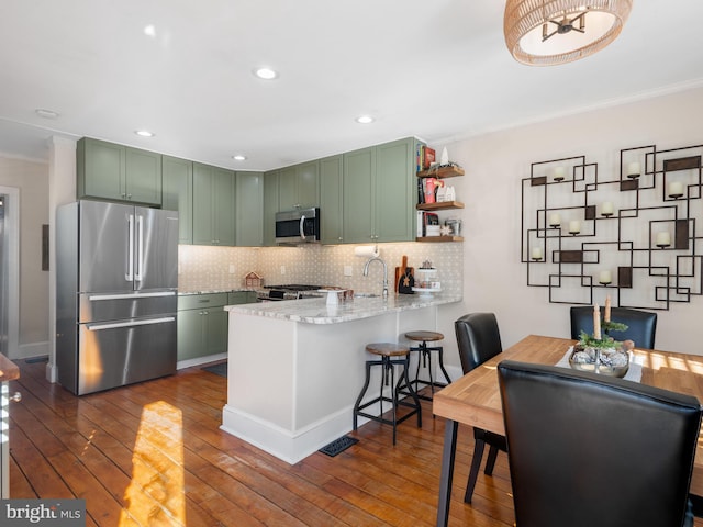 kitchen with dark hardwood / wood-style floors, kitchen peninsula, appliances with stainless steel finishes, and green cabinetry