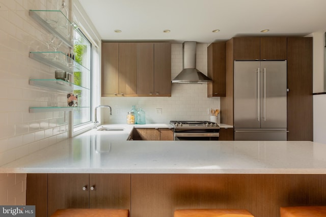 kitchen with stainless steel appliances, sink, light stone counters, backsplash, and wall chimney range hood