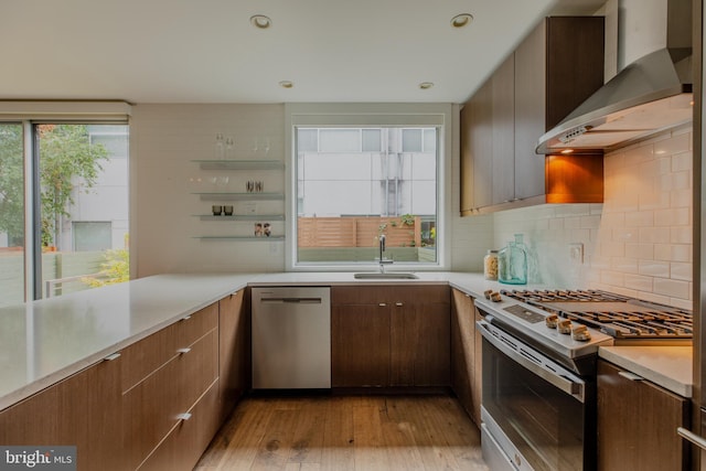 kitchen featuring sink, light wood-type flooring, tasteful backsplash, wall chimney range hood, and appliances with stainless steel finishes