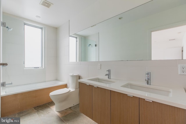 full bathroom featuring tile walls, toilet, decorative backsplash, vanity, and tiled shower / bath combo