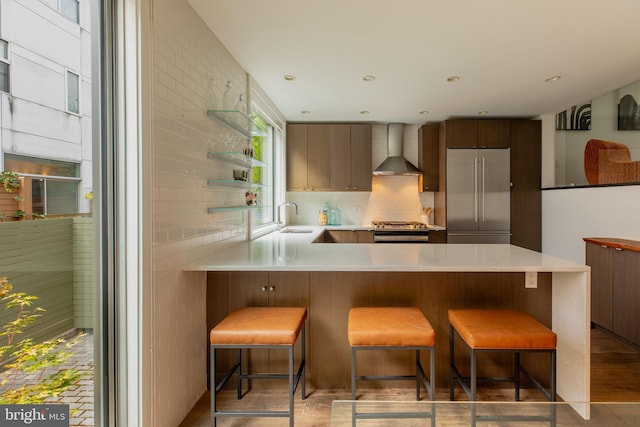 kitchen with stainless steel appliances, kitchen peninsula, a kitchen bar, sink, and wall chimney range hood