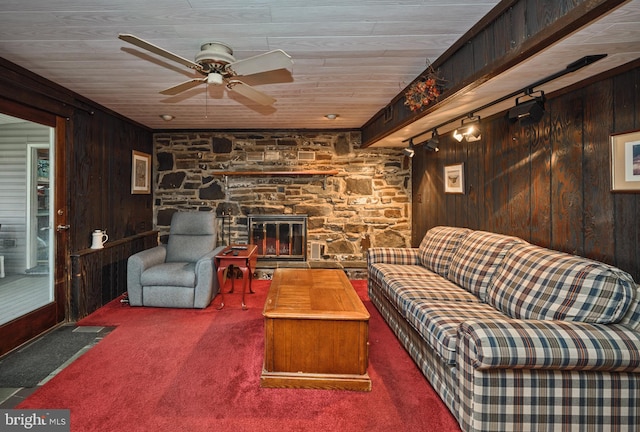 living room with beamed ceiling, a stone fireplace, carpet floors, and wooden walls