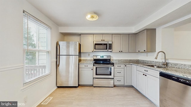 kitchen with sink, gray cabinets, appliances with stainless steel finishes, light hardwood / wood-style floors, and light stone counters