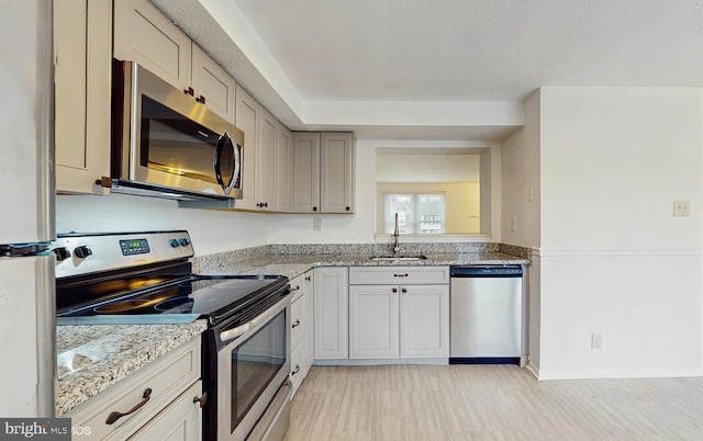 kitchen featuring light stone countertops, sink, light hardwood / wood-style floors, a textured ceiling, and appliances with stainless steel finishes