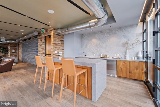 kitchen with light wood-type flooring, refrigerator, tasteful backsplash, and a kitchen breakfast bar