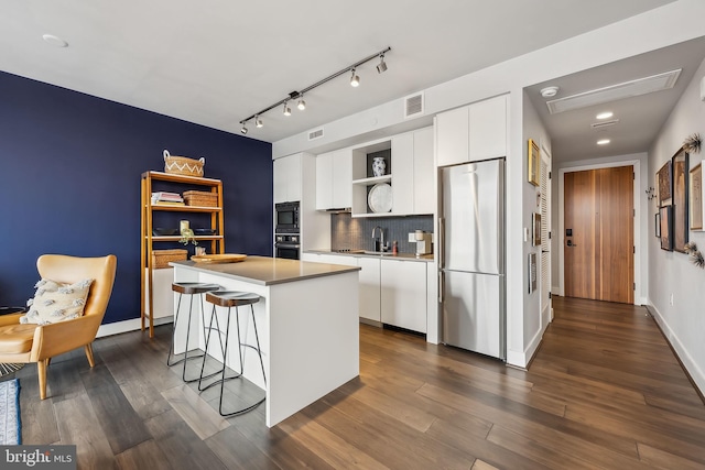 kitchen with appliances with stainless steel finishes, white cabinets, dark wood-type flooring, a center island, and a breakfast bar area