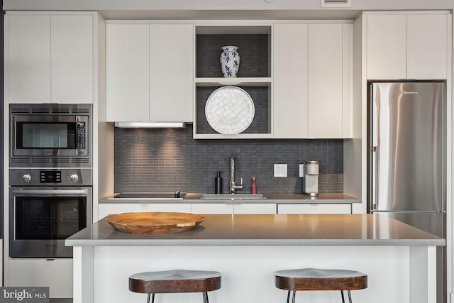 kitchen with white cabinetry, decorative backsplash, a kitchen breakfast bar, sink, and stainless steel appliances