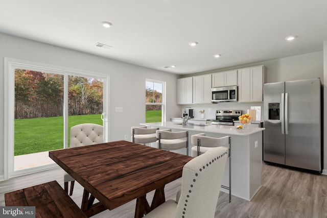 kitchen featuring white cabinetry, stainless steel appliances, light hardwood / wood-style floors, a kitchen bar, and a kitchen island with sink