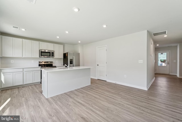 kitchen with sink, light hardwood / wood-style floors, a kitchen island with sink, white cabinets, and appliances with stainless steel finishes