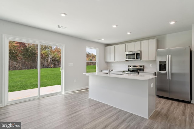 kitchen featuring sink, stainless steel appliances, a center island with sink, white cabinets, and light wood-type flooring