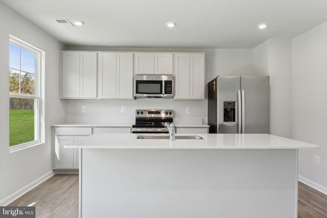 kitchen featuring white cabinets, a kitchen island with sink, appliances with stainless steel finishes, and light hardwood / wood-style flooring