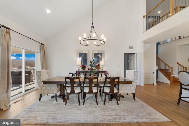 dining area featuring wood-type flooring, a high ceiling, and a notable chandelier