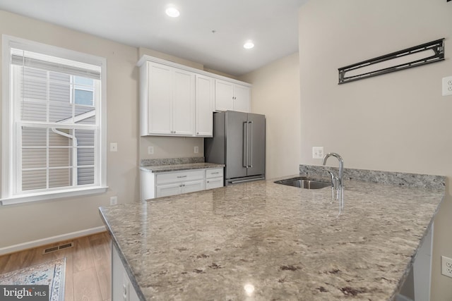 kitchen with high end fridge, light stone countertops, and white cabinetry