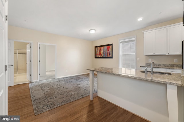 kitchen with white cabinets, dark hardwood / wood-style flooring, light stone countertops, and sink