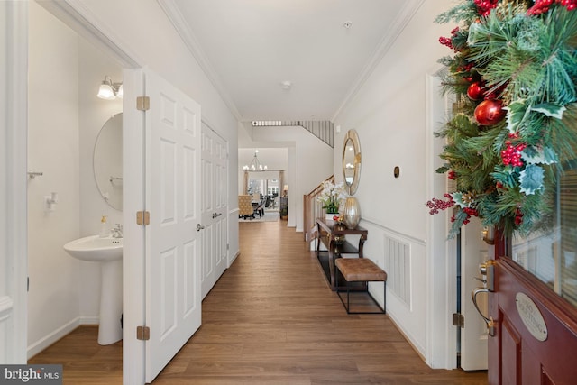 corridor with sink, wood-type flooring, crown molding, and a chandelier