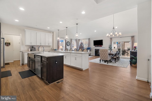 kitchen with vaulted ceiling, a kitchen island with sink, sink, pendant lighting, and white cabinetry