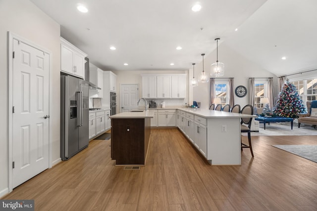 kitchen with kitchen peninsula, appliances with stainless steel finishes, a kitchen breakfast bar, decorative light fixtures, and white cabinets