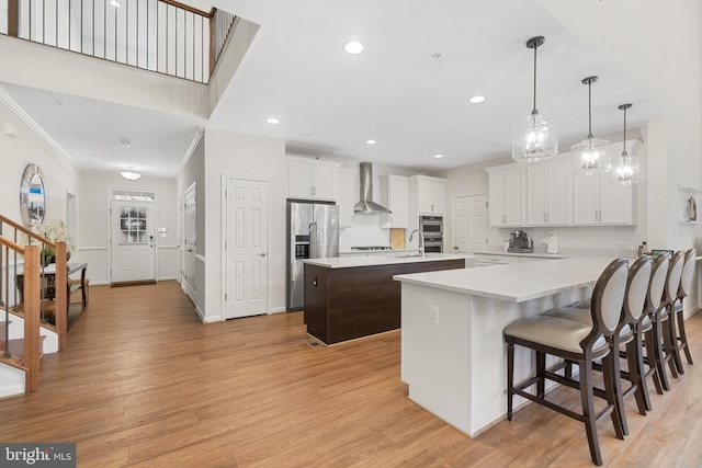 kitchen with wall chimney range hood, appliances with stainless steel finishes, decorative light fixtures, a kitchen island, and white cabinetry