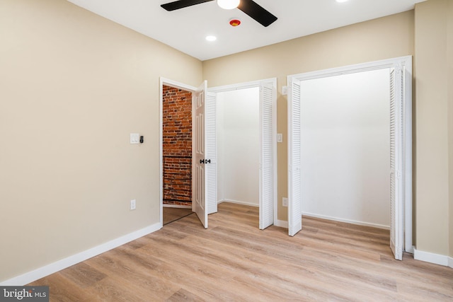 unfurnished bedroom with light wood-type flooring, two closets, and ceiling fan