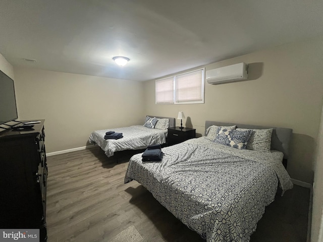 bedroom featuring a wall mounted air conditioner, baseboards, and wood finished floors