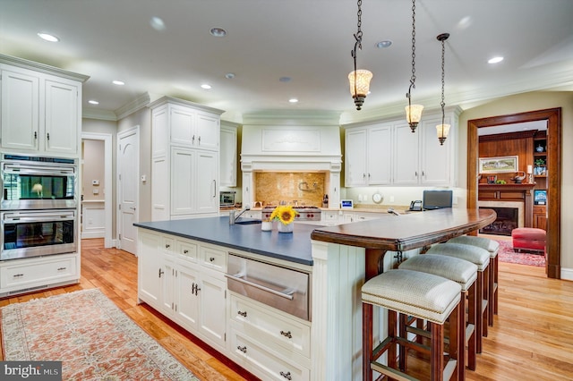 kitchen with white cabinetry, hanging light fixtures, light hardwood / wood-style flooring, appliances with stainless steel finishes, and ornamental molding