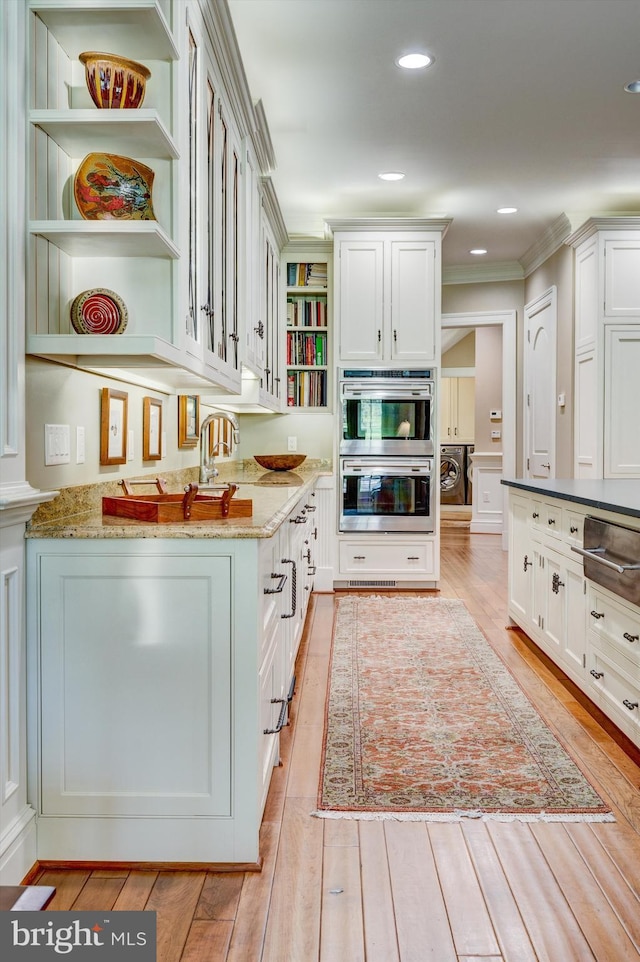 kitchen with light stone countertops, ornamental molding, double oven, light hardwood / wood-style floors, and white cabinetry