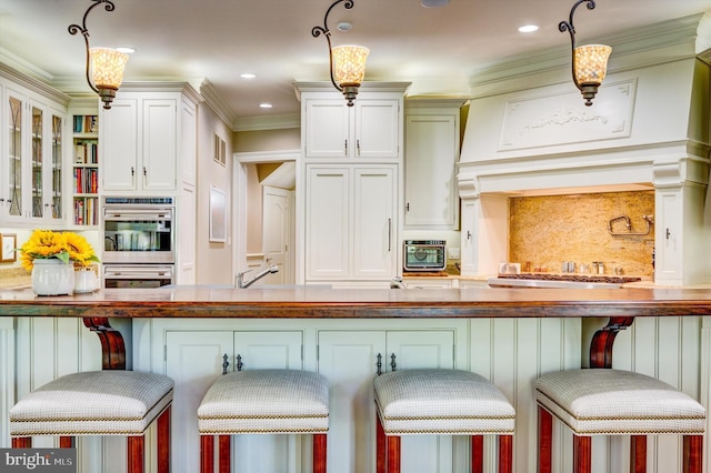 kitchen featuring white cabinets, a kitchen breakfast bar, ornamental molding, and decorative light fixtures